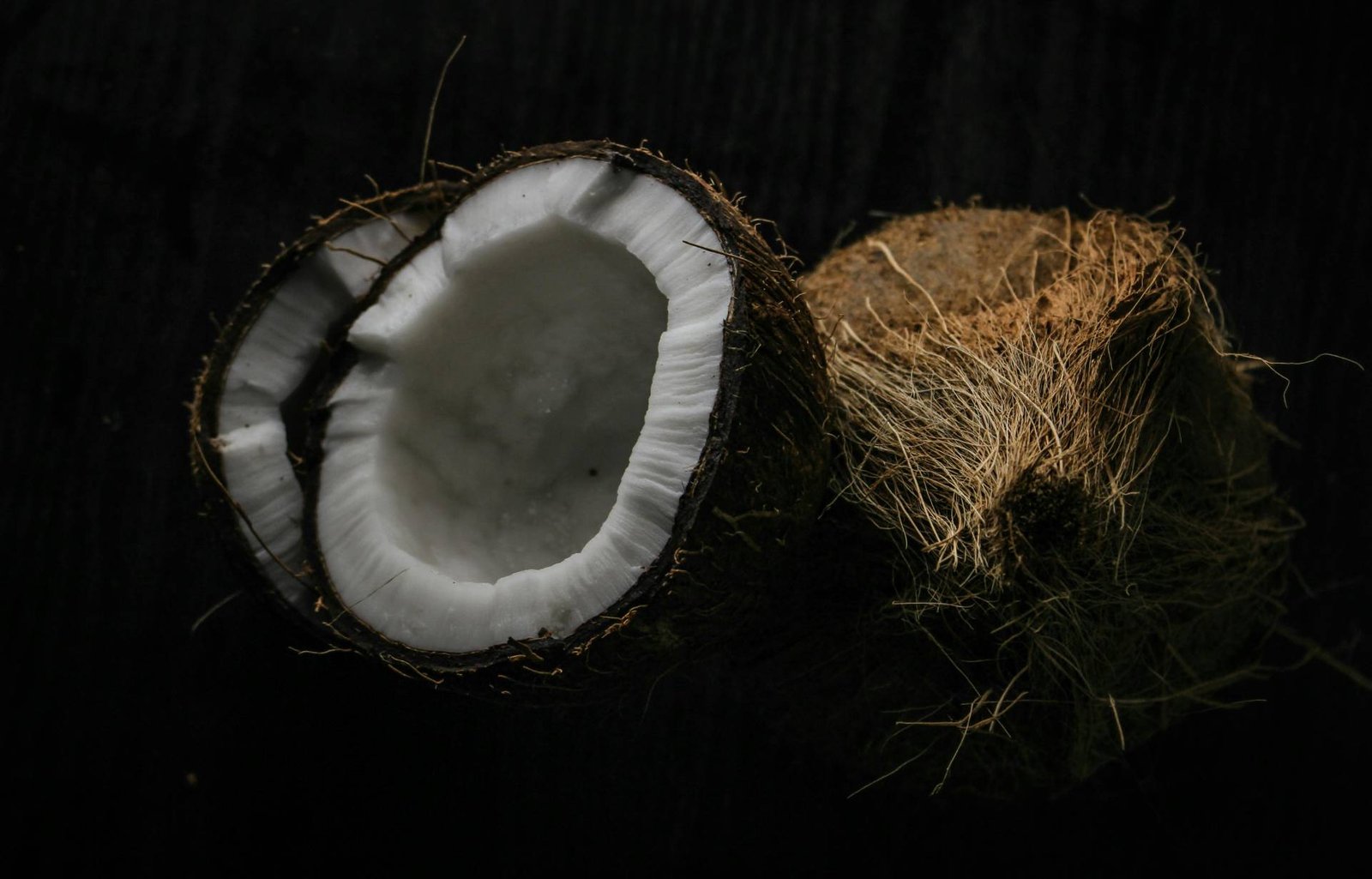 Detailed view of a fresh halved coconut showcasing its texture against a dark background.